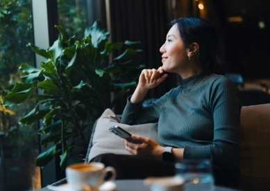 Young Woman with Smartphone Looking Out Cafe Window